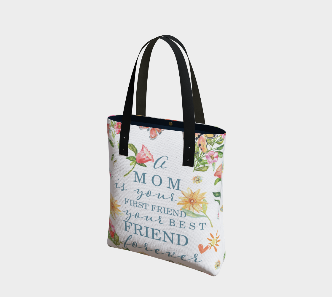 Alternate angle view of bag. white cloth tote bag with various hand painted flowers in pink and yellow with green leaves. The words "A mom is your first friend your best friend forever" in a light blue font. The bad is adorned with a vegan leather strap shown in black