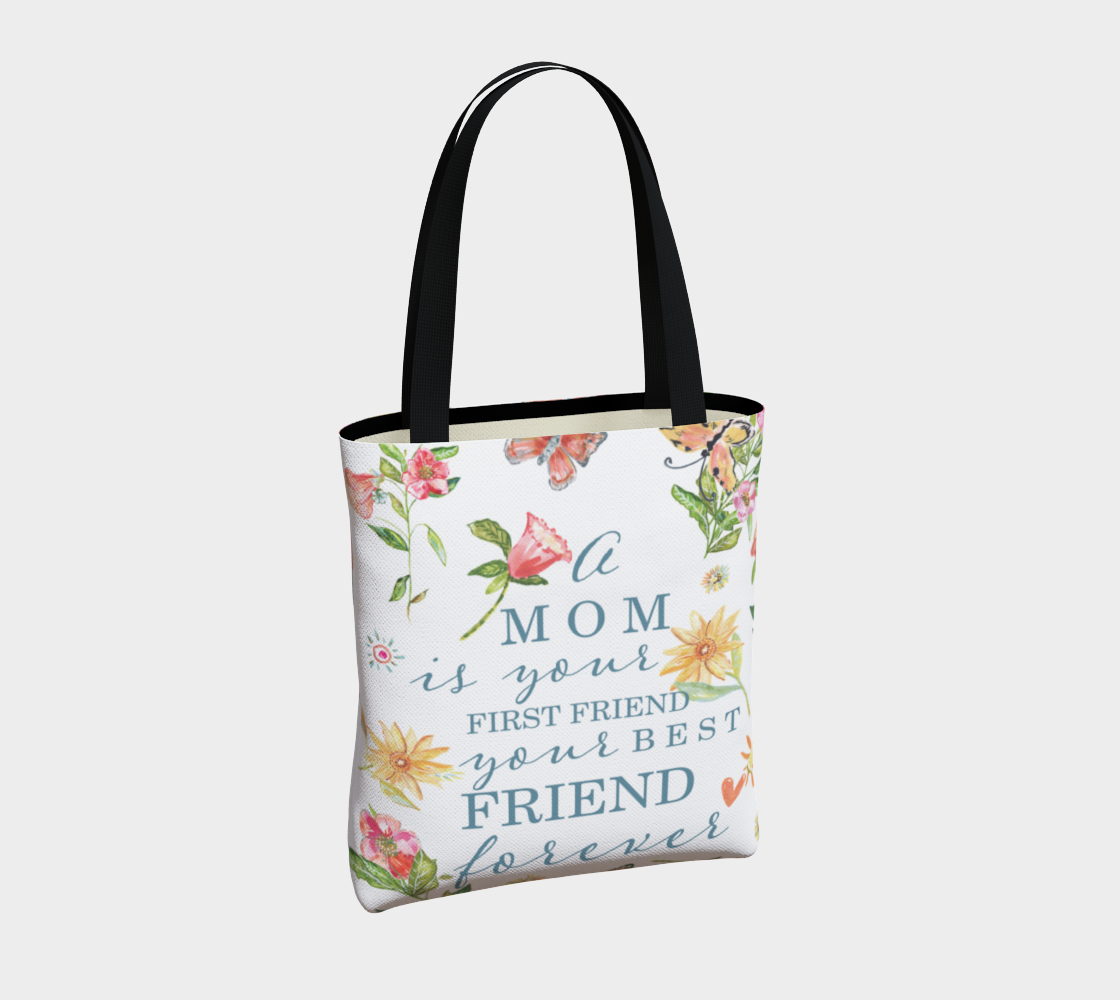 Alternate angle view of bag. white cloth tote bag with various hand painted flowers in pink and yellow with green leaves. The words "A mom is your first friend your best friend forever" in a light blue font. The bad is adorned with a vegan leather strap shown in black